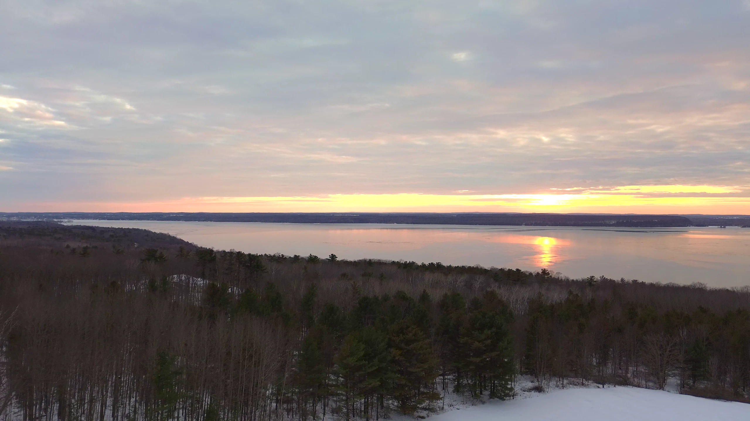 Soft sunset reflected over a lake beyond a wooded ridgeline